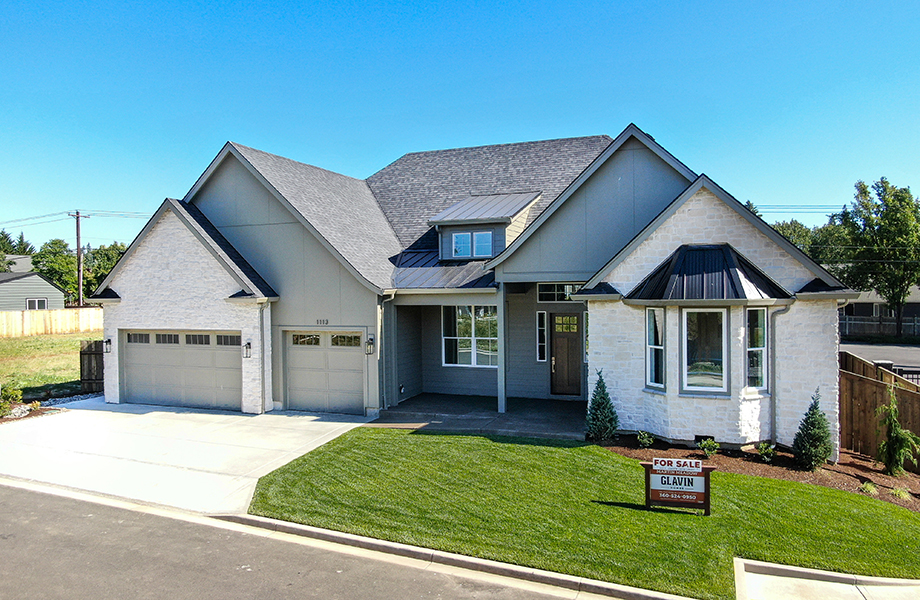 Exterior of one-level home, light brick accents. Landscaped yard with grass, shrubs, and river rock. For sale sign, built by Glavin Homes. Martin Meadow Lot 1